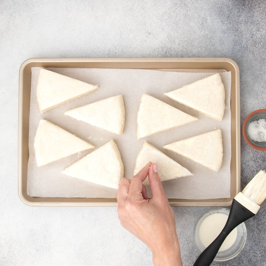 fingers sprinkling coarse sugar on top of raw scone triangle