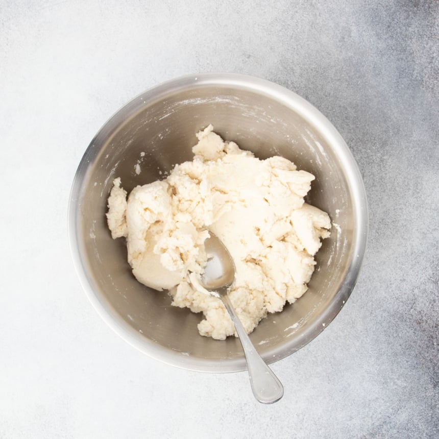 Gluten free scone dough fully mixed and rough in texture in a metal bowl with spoon
