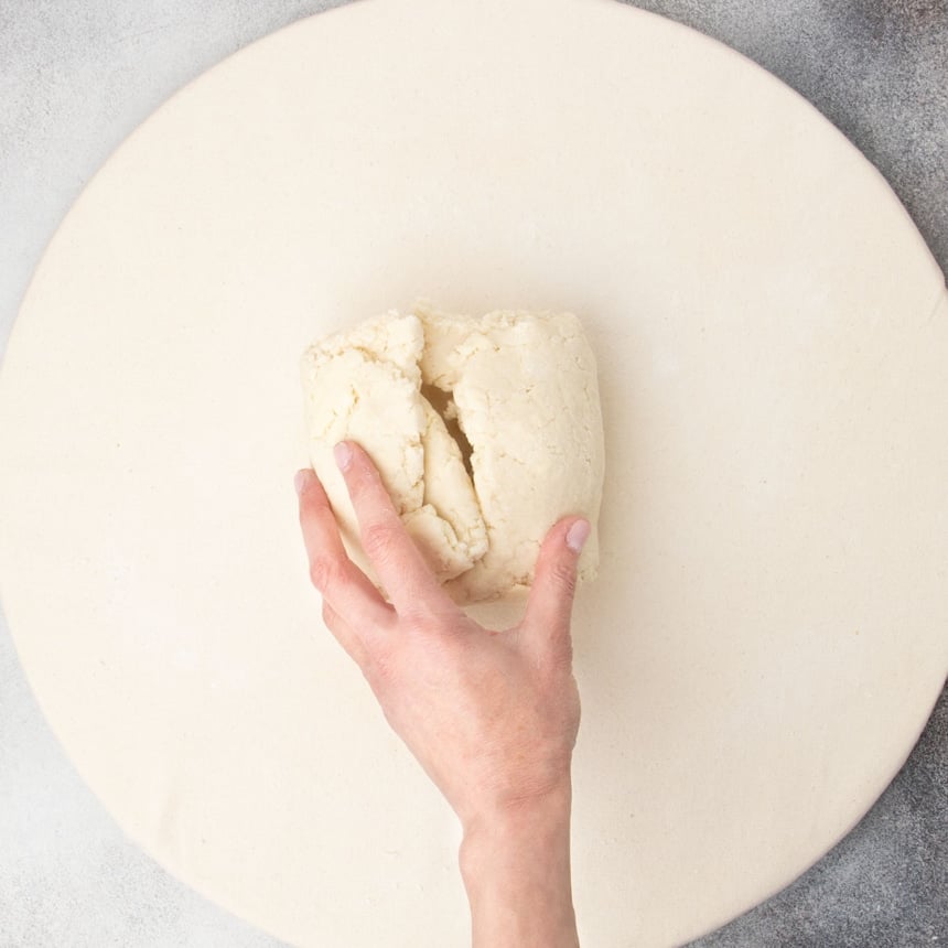 hand holding together folded dough into square packet on tan cloth