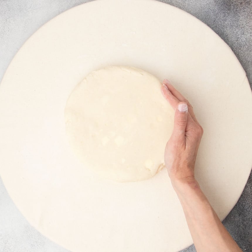 hand shaping tan raw scone dough into a round on tan cloth