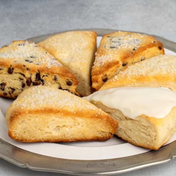 Assorted gluten free scones on a plate, including plain, chocolate chip, and one with vanilla glaze