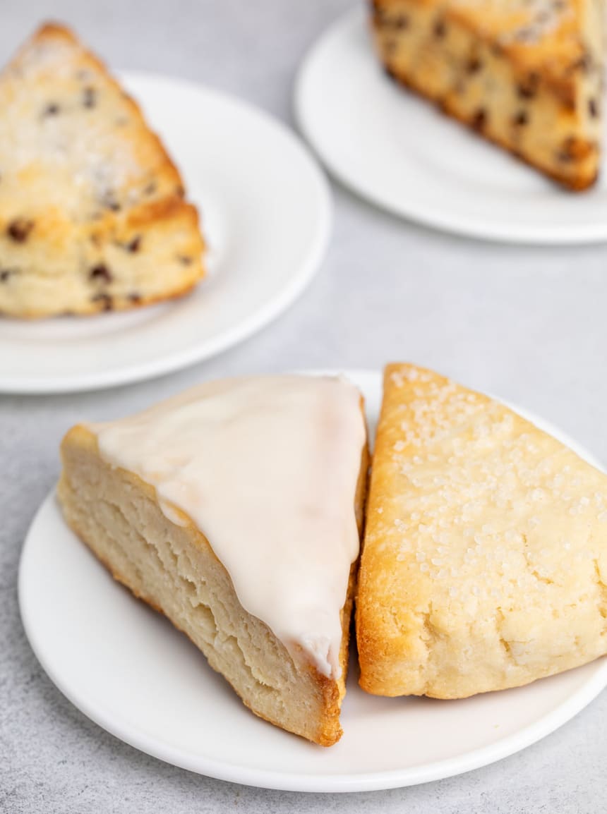 Two gluten free scones on a white plate, one glazed and one topped with coarse sugar