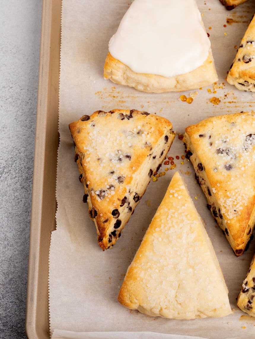 Freshly baked gluten free scones, including chocolate chip and glazed, on a parchment-lined tray