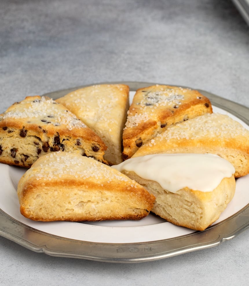 Assorted gluten free scones on a plate, including plain, chocolate chip, and one with vanilla glaze