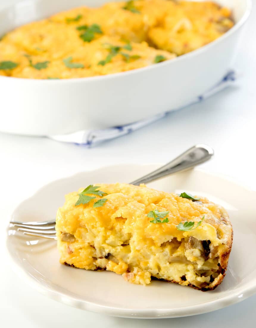 yellow rectangular slice of breakfast casserole with mushrooms inside and green parsley leaves on top on small white plate with small metal fork