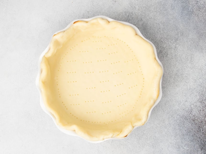 Shaped and parbaked gluten free pie crust in a white ceramic dish with crimped edges and docked bottom.