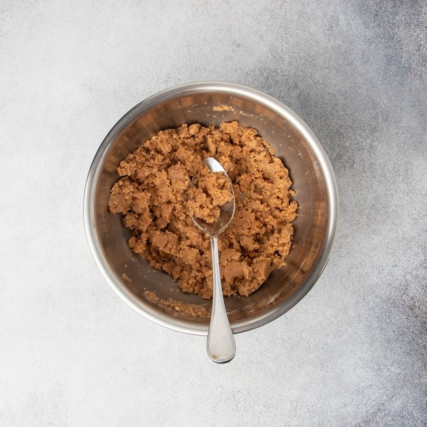 Coarse, sandy raw brown crumb topping mixture in a bowl with a spoon.