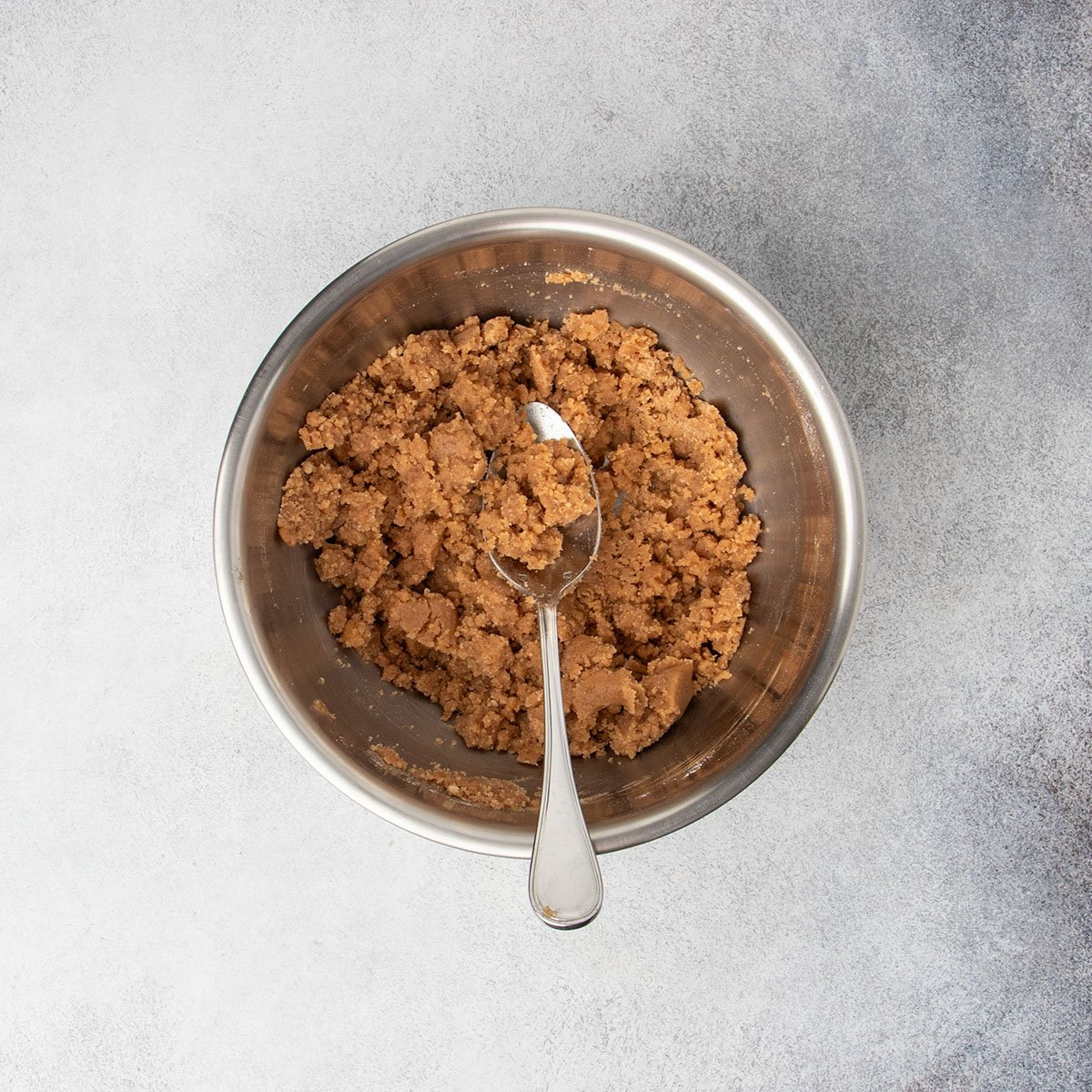 Coarse, sandy raw brown crumb topping mixture in a bowl with a spoon.