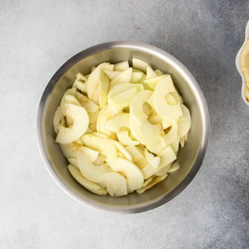 Freshly peeled and cored, thinly sliced green apples in a large metal mixing bowl.