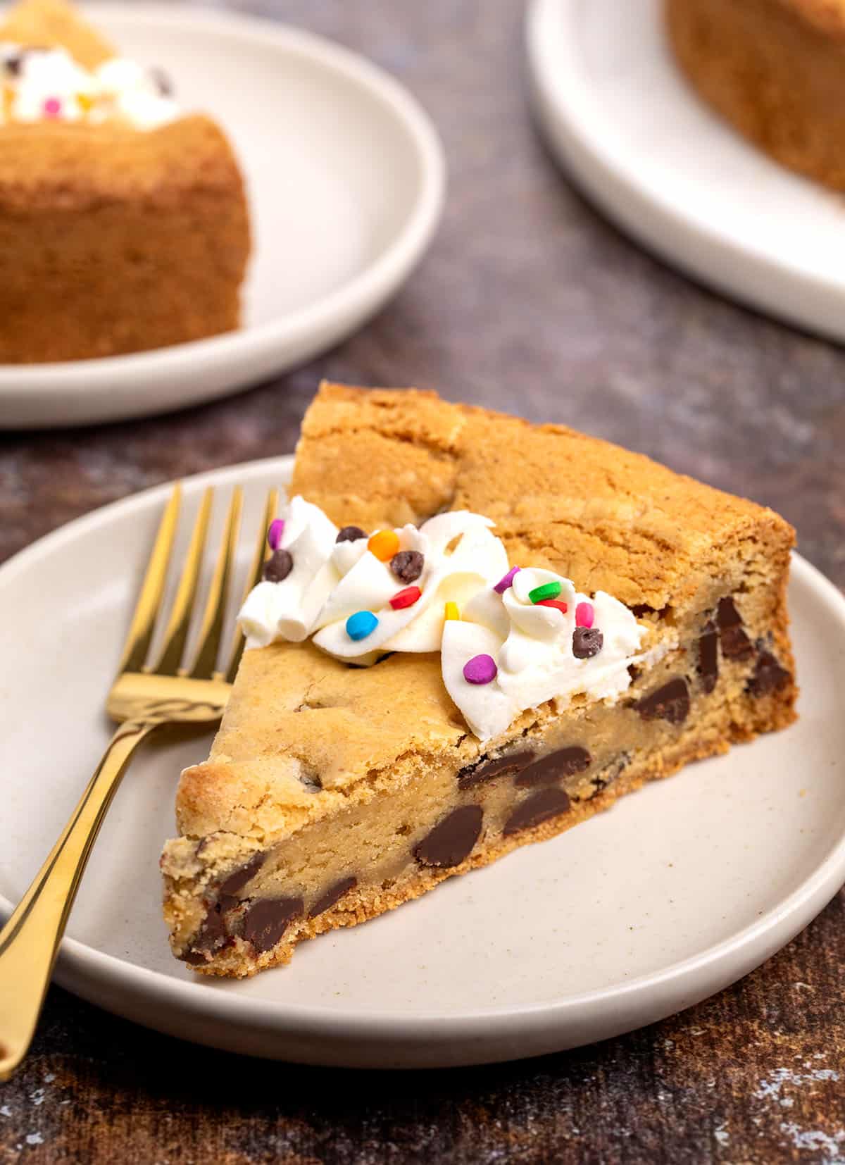 Side view of a slice showing the soft texture and chocolate chips inside, topped with piped frosting and sprinkles.