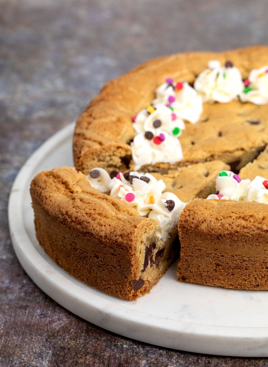 Closeup of sliced cookie cake on a marble platter, showing golden edges and soft interior with chocolate chips.