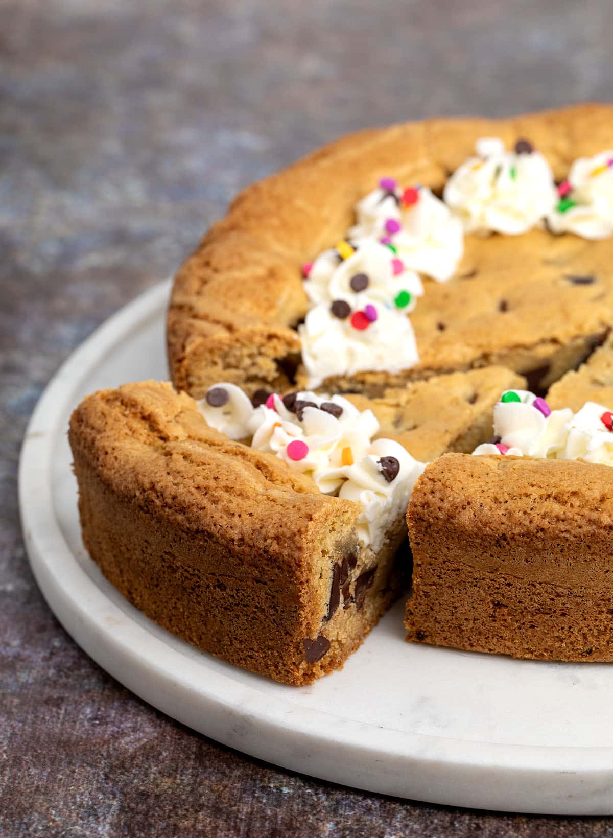 Closeup of sliced cookie cake on a marble platter, showing golden edges and soft interior with chocolate chips.