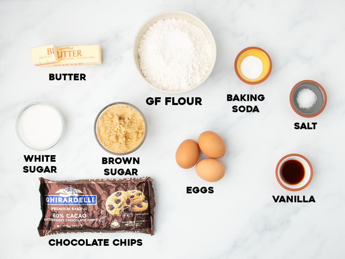 Flat lay of labeled ingredients for gluten free cookie cake, including gluten free flour, butter, sugars, chocolate chips, and vanilla.