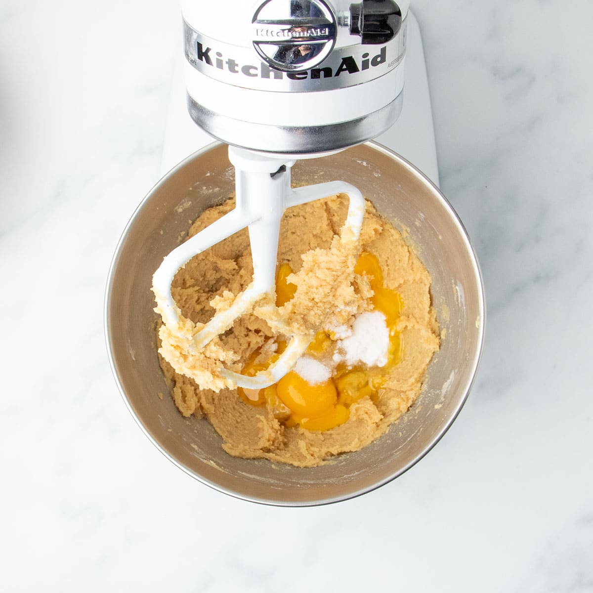 Egg, egg yolks, and leavening added to creamed butter-sugar mixture in a stand mixer.