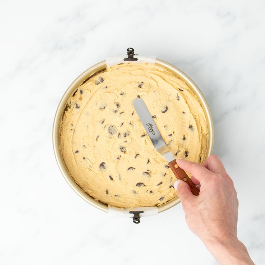 Hand smoothing dough evenly in the pan using an offset spatula with a brown handle