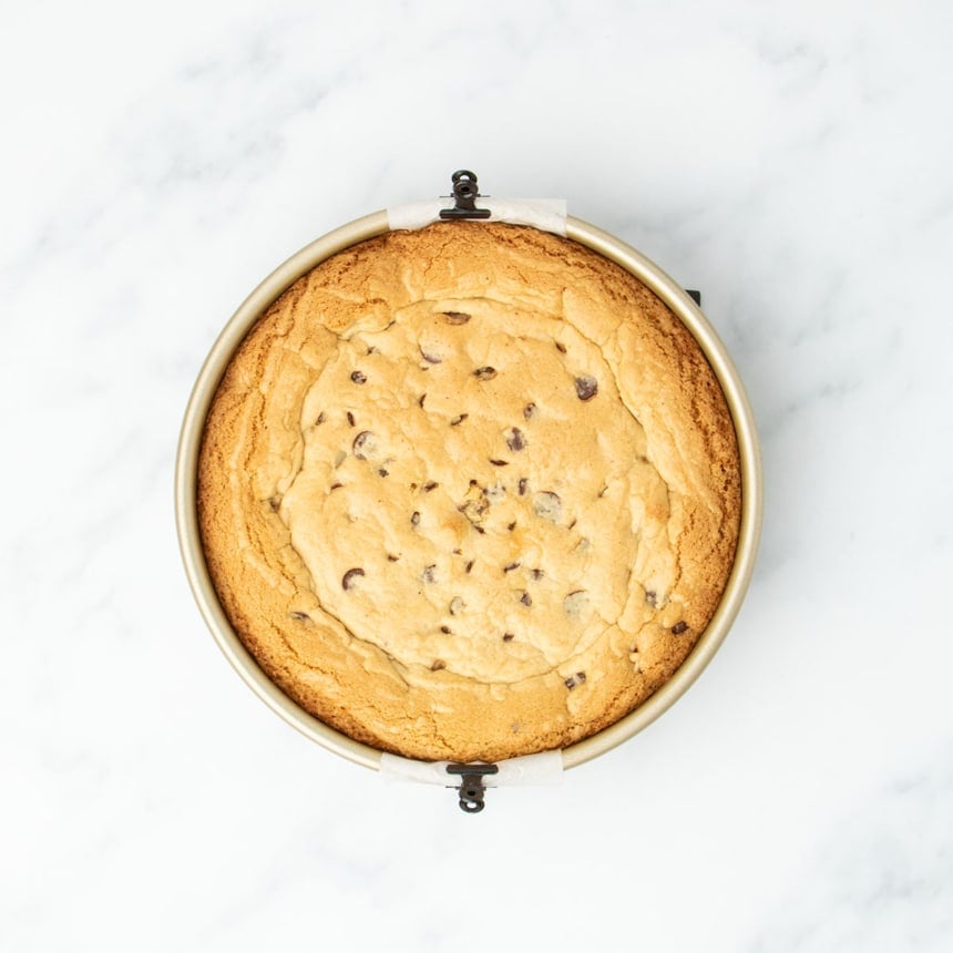 Fully baked gluten free cookie cake in the pan, golden brown and puffed with a crackled top