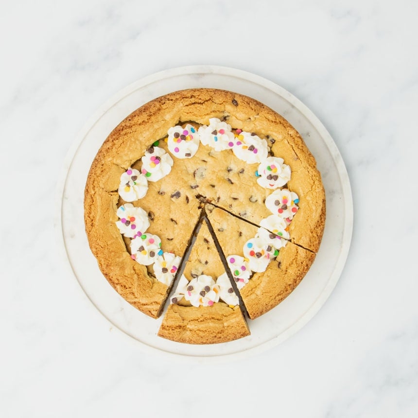 Cooled and decorated cookie cake with piped frosting rosettes and sprinkles, one slice partially pulled out
