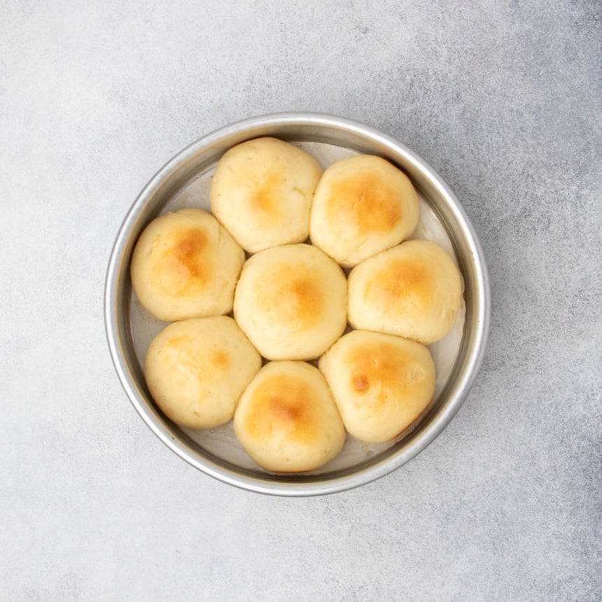 Freshly baked gluten free dinner rolls in a round pan with golden brown tops.