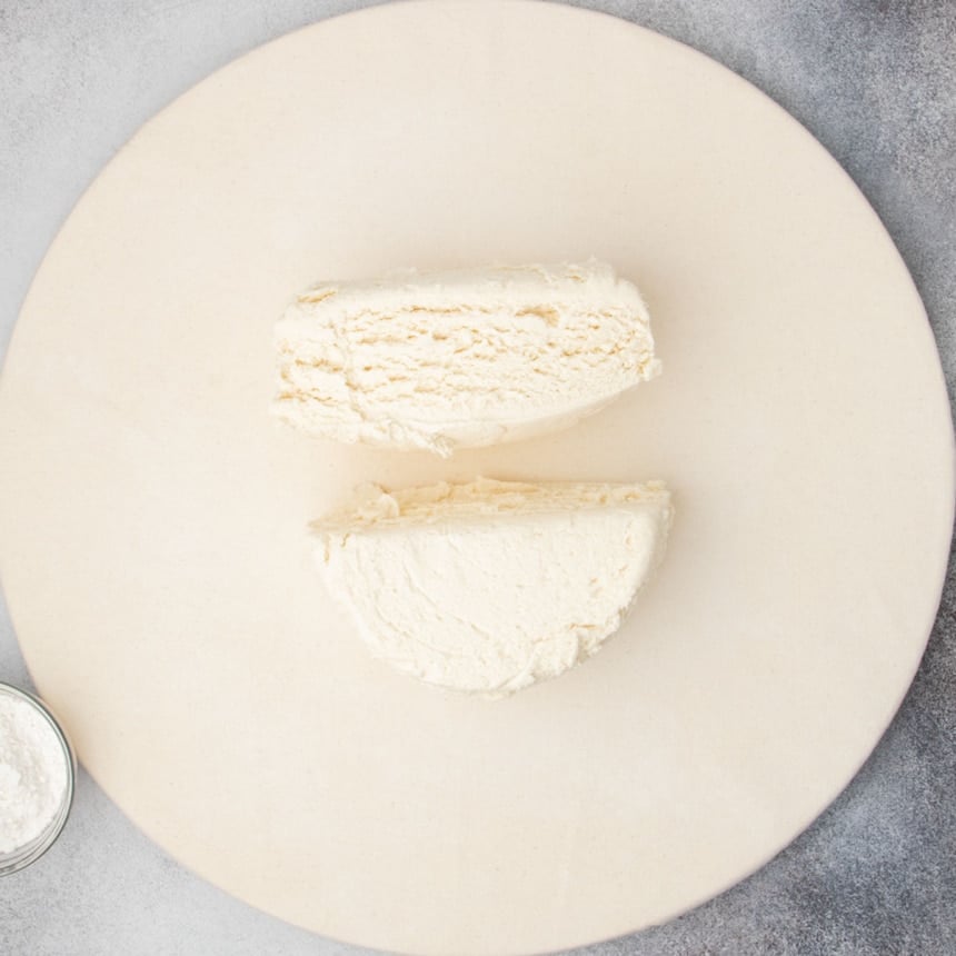 Chilled round of raw proofed dough cut in half on a floured surface.