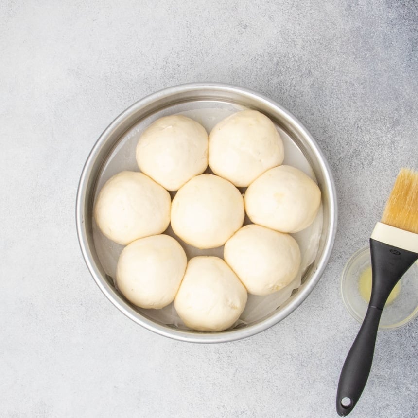 Raw round rolls after proofing in a round pan, brushed with butter and ready to bake.
