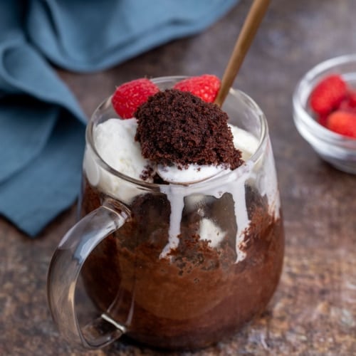 Spoonful of rich chocolate cake lifted from a glass mug, served with vanilla ice cream and raspberries.