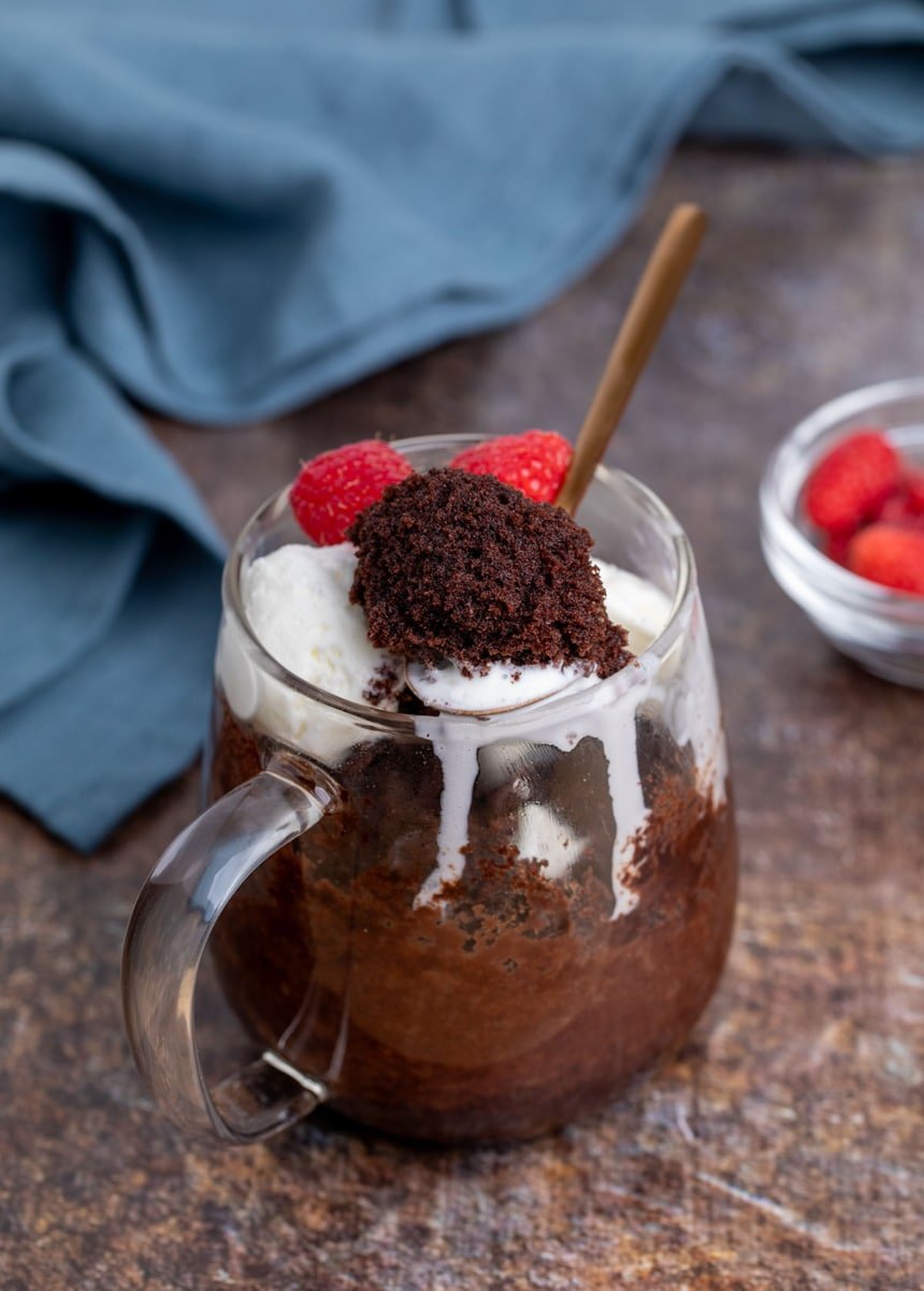 Overhead view of a gluten free chocolate mug cake topped with ice cream and fresh raspberries.