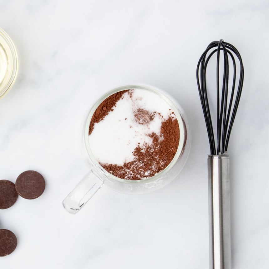 Dry ingredients added to a clear mug, including sugar and cocoa powder.