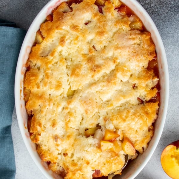 Overhead view of a freshly baked gluten free peach cobbler with crisp golden topping and bubbling fruit at the edges.