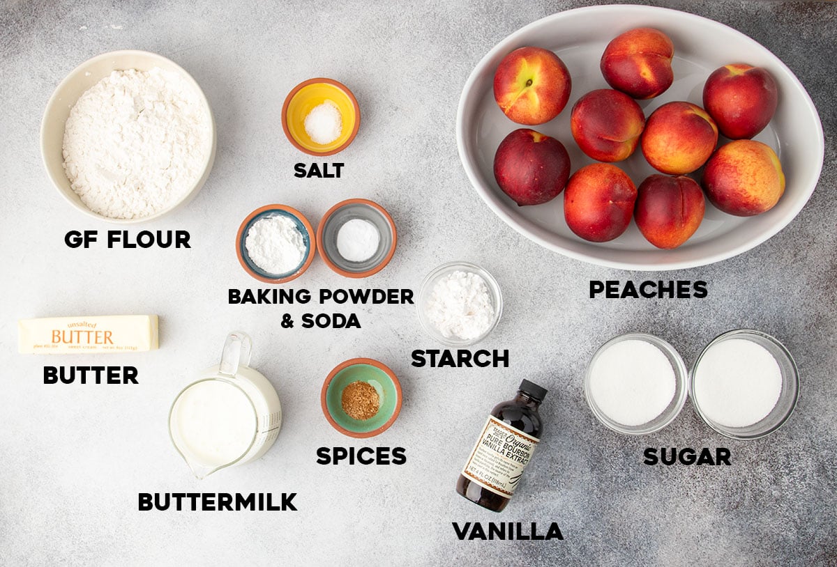 Labeled ingredients laid out for making peach cobbler, including gluten free flour, sugar, butter, fresh peaches, and vanilla.