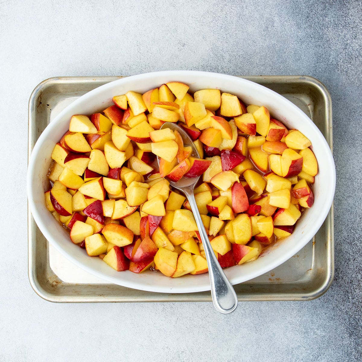 Softened peach filling in the baking dish after a short pre-bake, mixed with a large metal spoon, ready for the topping.