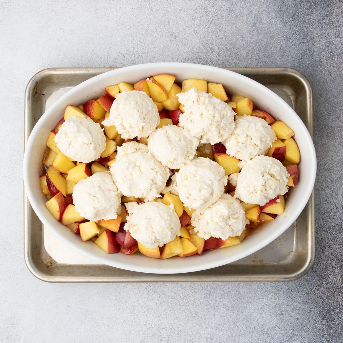 Scoops of raw luten free cobbler topping arranged over warm peaches in the baking dish.