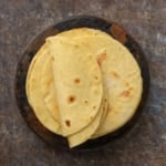 Overhead view of freshly cooked almond flour tortillas stacked on a round wooden plate