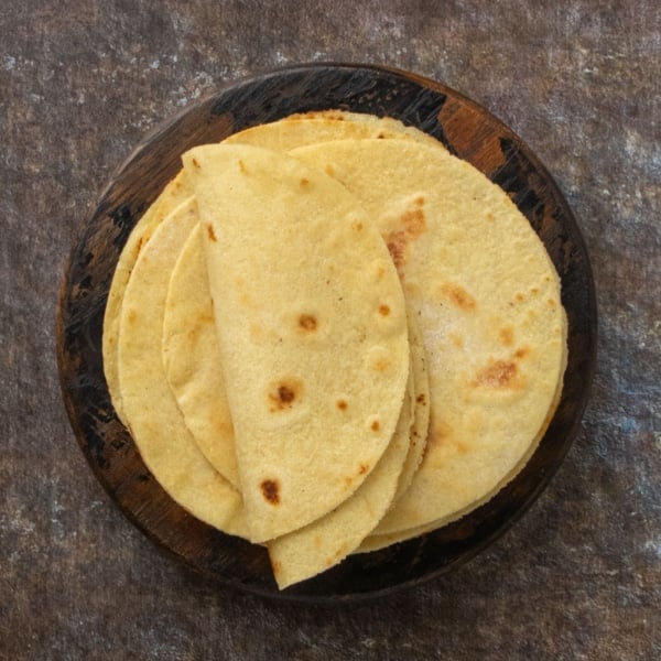 Overhead view of freshly cooked almond flour tortillas stacked on a round wooden plate