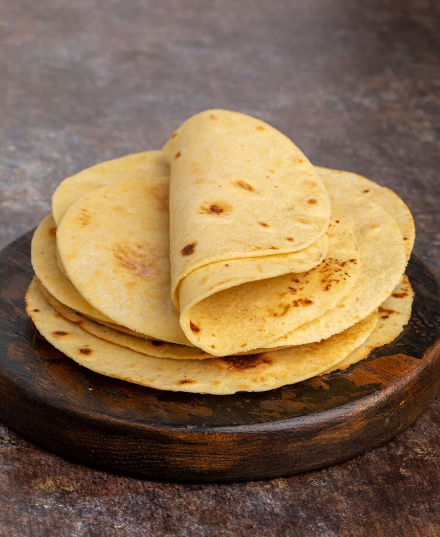 Side angle of warm tortillas stacked and folded slightly on a wooden board