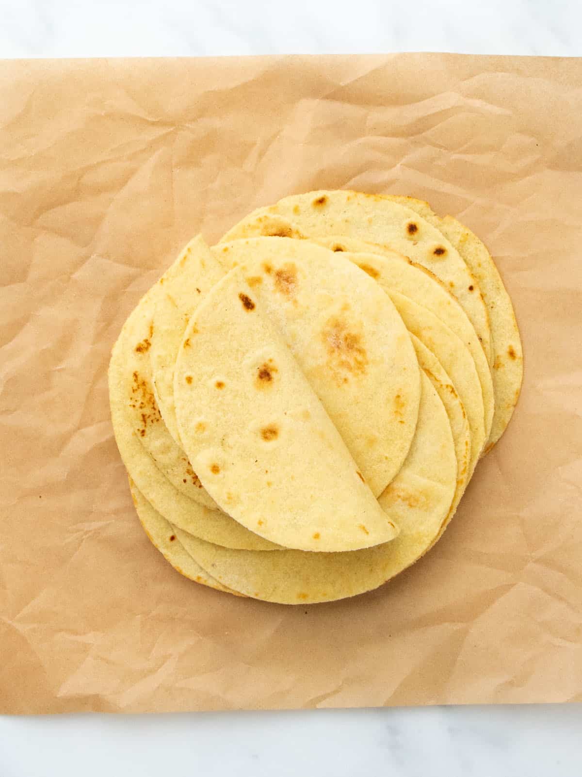 A stack of tortillas on brown parchment paper with a few edges folded upward.