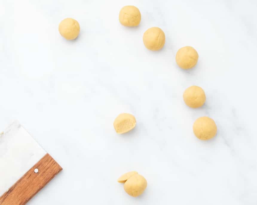 Round balls of raw dough waiting to be shaped with one ball reapportioned to make shaping easier