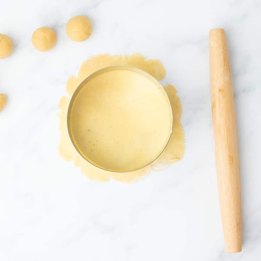 Round metal cutter placed over thinly rolled dough sheet