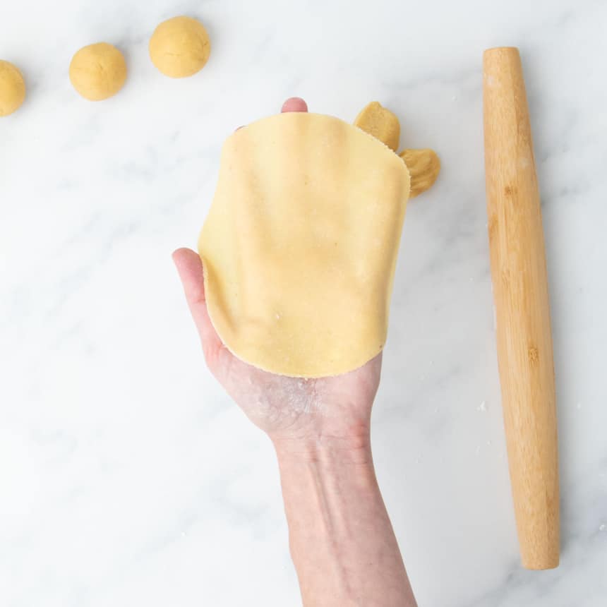 Uncooked tortilla held in hand, showing its flexibility and thinness