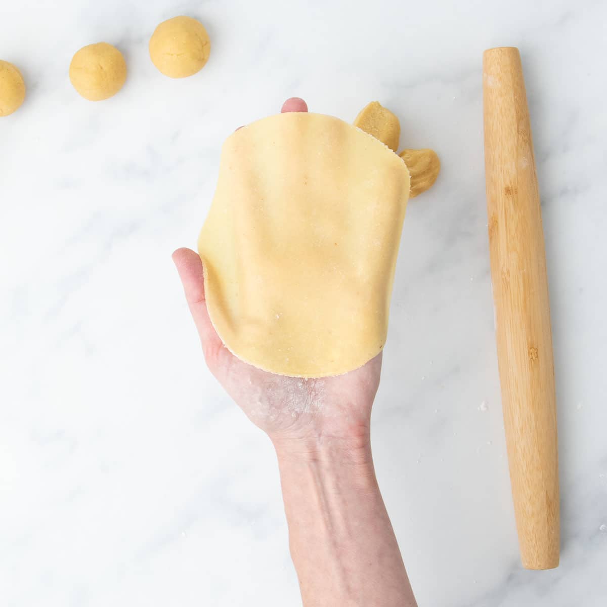 Uncooked tortilla held in hand, showing its flexibility and thinness.