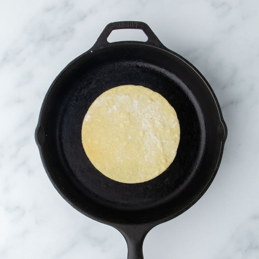 Almond flour tortilla placed in a hot cast iron skillet for cooking