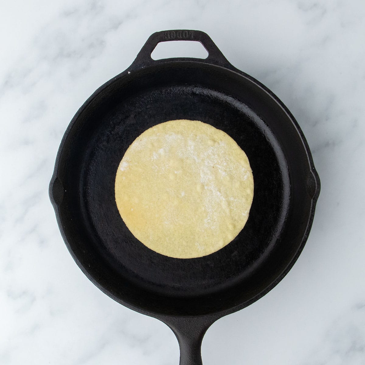 Tortilla placed in a hot cast iron skillet for cooking.
