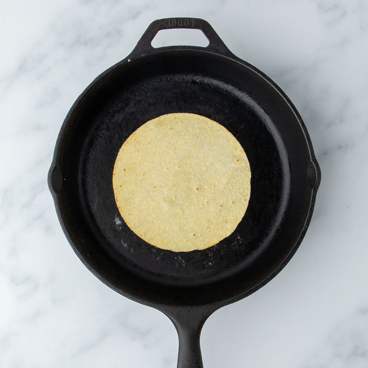 Lightly golden tortilla just after being flipped in skillet.