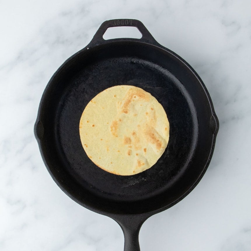 A single almond flour tortilla cooking in a black cast iron skillet on a marble surface