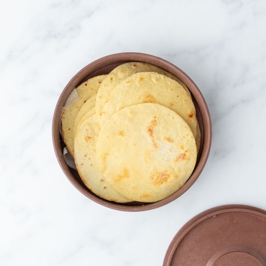 A stack of cooked almond flour tortillas nestled in a brown container, viewed from above
