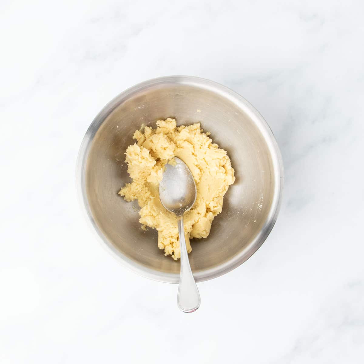 Mixed dough for tortillas in a metal bowl with a spoon.