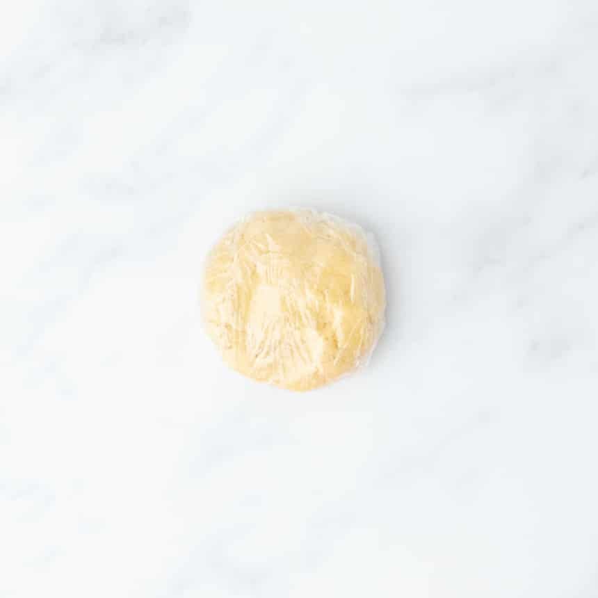 Round dough ball wrapped in plastic wrap, resting on a clean counter