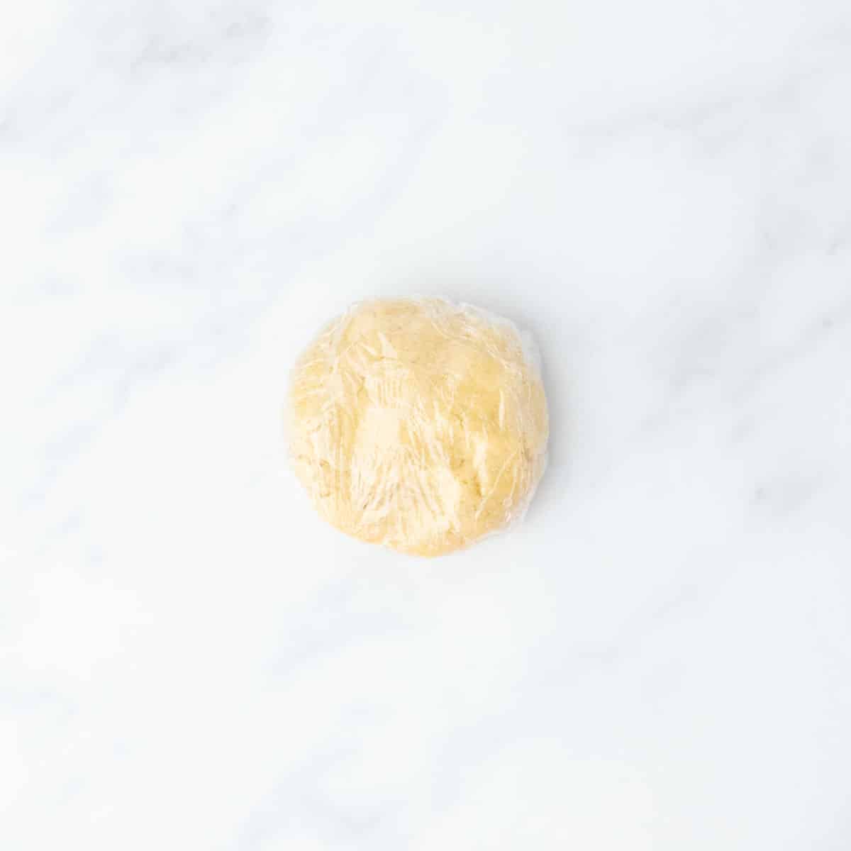 Round dough ball wrapped in plastic wrap, resting on a clean counter.
