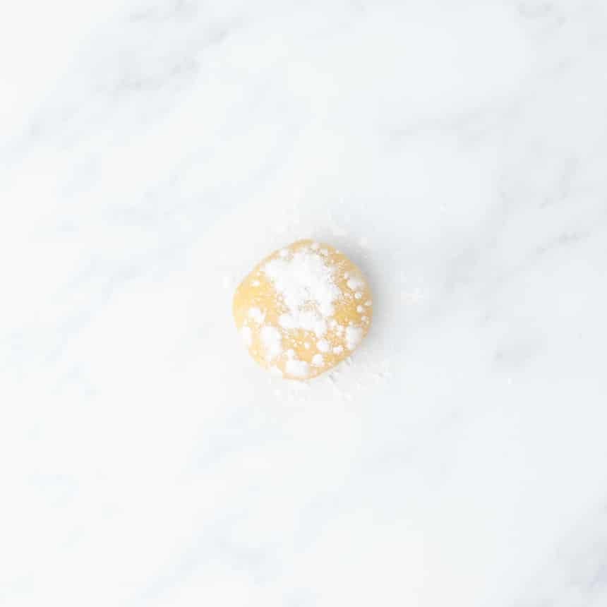 A small ball of dough dusted with gluten free flour, resting on a white marble surface