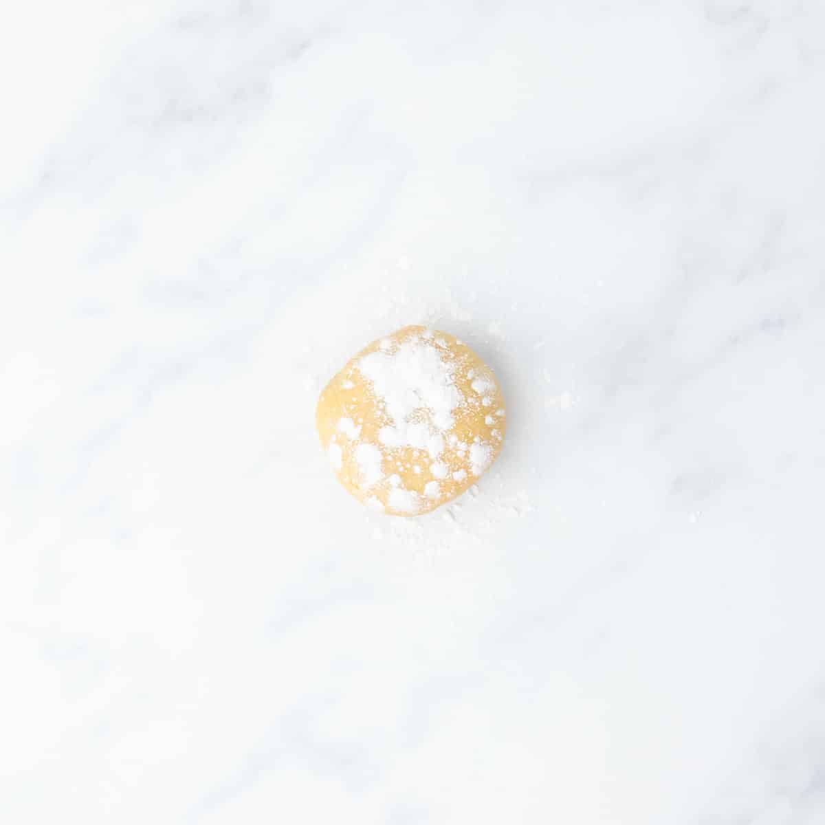 A small ball of dough dusted with gluten free flour, resting on a white marble surface.