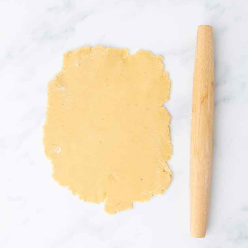 Dough rolled into a rough rectangle next to a wooden rolling pin